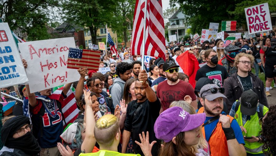 A man waves an American flag in a crowd of protesters holding homemade signs